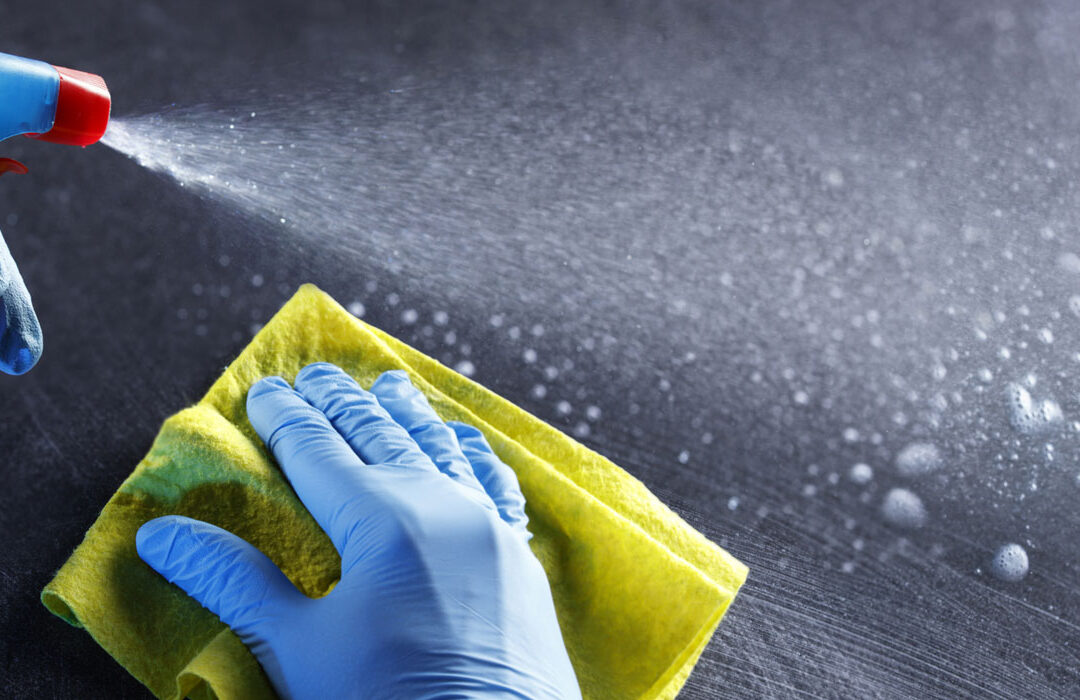 gloved hands with spray bottle and cleaning cloth