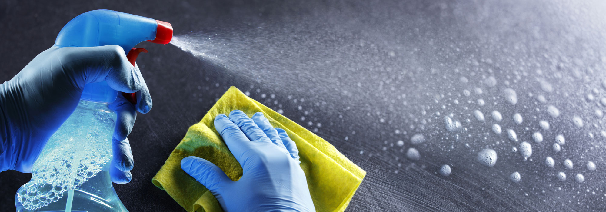 gloved hands with spray bottle and cleaning cloth